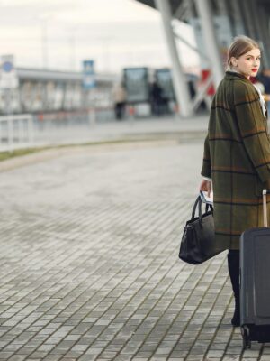 Back view of trendy businesswoman carrying baggage before flight near airport building